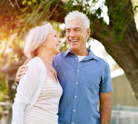An older man and woman standing outside and smiling after receiving dental implants in Lady Lake