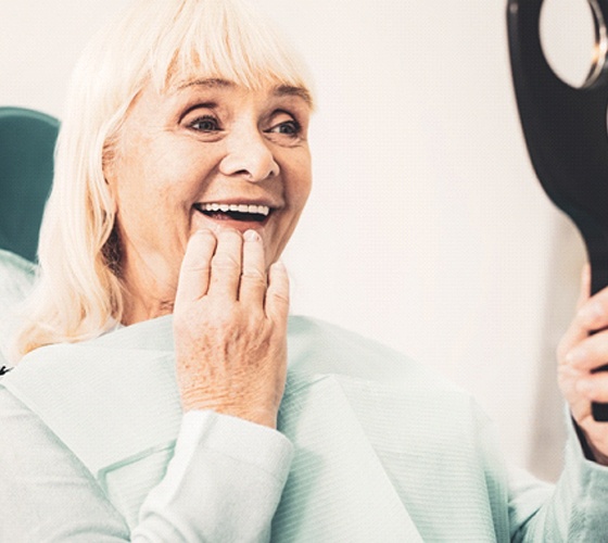 Senior woman checking her new dentures in handheld mirror