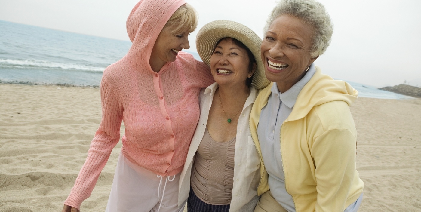 Three senior women laughing together on the beach
