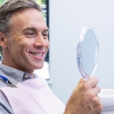 Man in dental chair looking at his smile in mirror