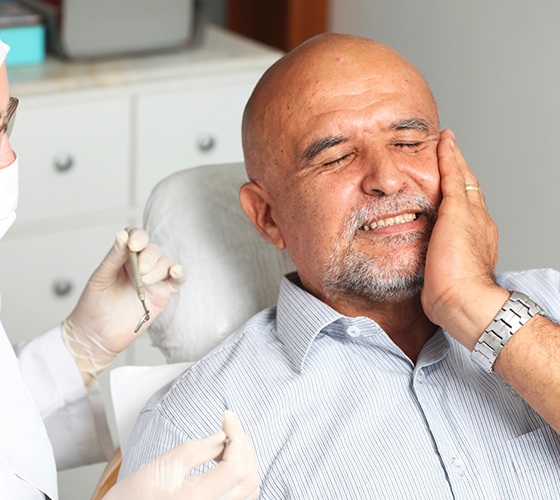 Man in need of tooth extraction holding cheek in pain