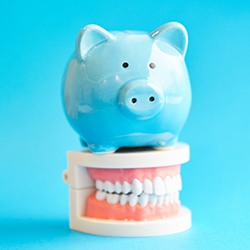 Piggy bank atop model teeth representing the cost of cosmetic dentistry in Lady lake