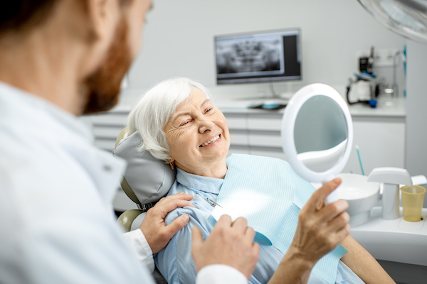 happy older woman smiling in mirror at dentist's office