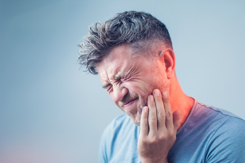 person holding their tooth and wincing in pain