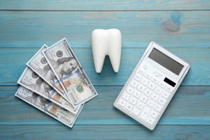 Fake tooth on a blue table next to dollar bills and a calculator